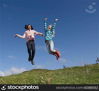 Two young girls jumping on hill