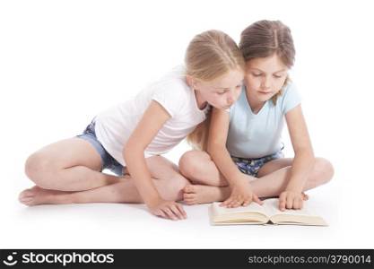 two young girls reading a book together in studio with white background