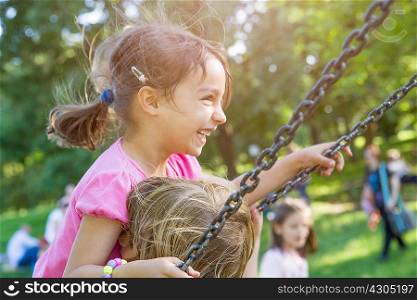 Two young girls swinging together on park swing