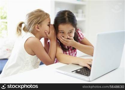 Two Young Girls Using Laptop At Home And Whispering