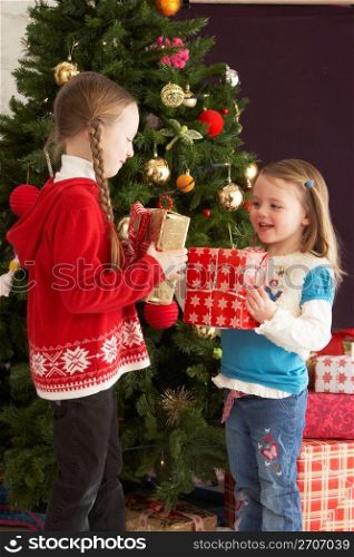Two Young Girls With Presents In Front Of Christmas Tree