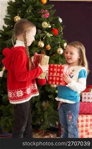 Two Young Girls With Presents In Front Of Christmas Tree