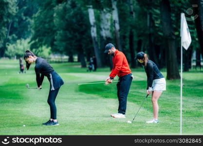 Two young golfers practicing chipping shots on a golf course with golf instructor