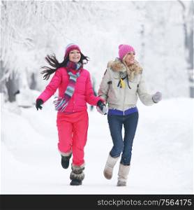 Two young happy smiling women running in the winter park. Two women running in winter park