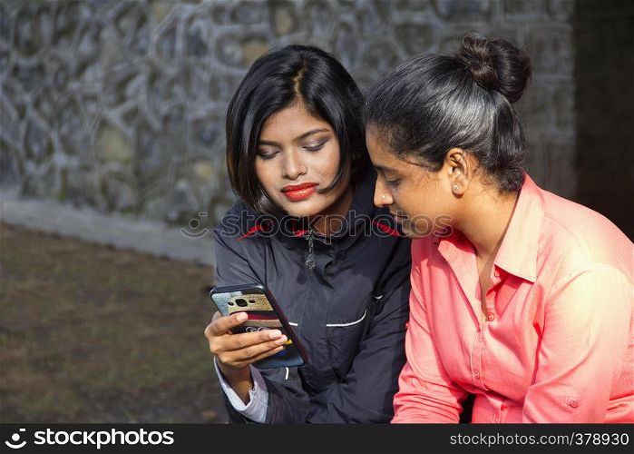 Two young Indian girls sitting and looking at their mobile, Pune. Two young Indian girls sitting and looking at their mobile, Pune.