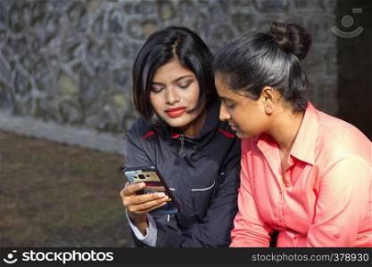 Two young Indian girls sitting and looking at their mobile, Pune. Two young Indian girls sitting and looking at their mobile, Pune.