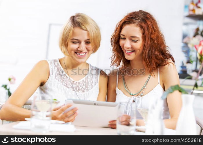 Two young ladies in cafe using tablet pc