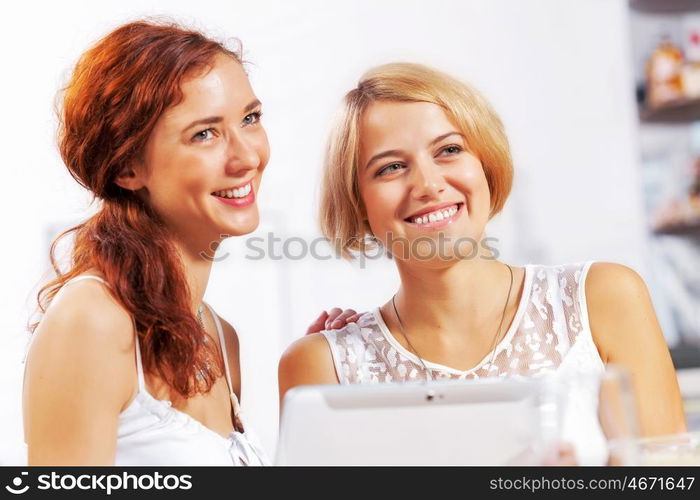 Two young ladies in cafe using tablet pc