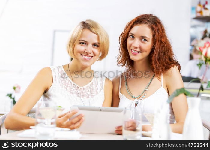 Two young ladies in cafe using tablet pc