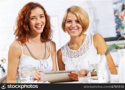 Two young ladies in cafe using tablet pc