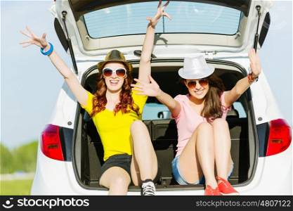 Two young ladies. Young happy young woman sitting in car trunk outdoor