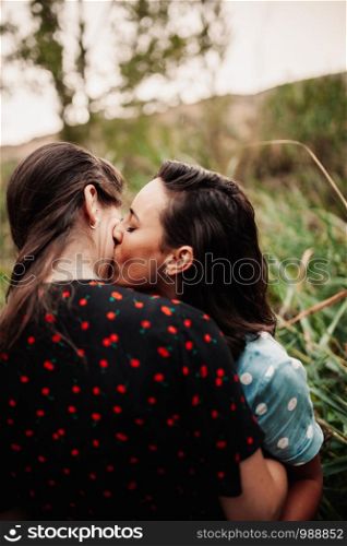 Two young lesbian women embraced kissing on the field wearing dresses