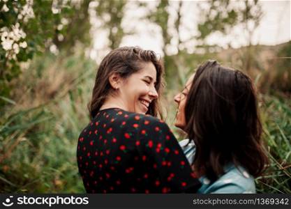 Two young lesbians look at each other an smiling in the field wearing dresses