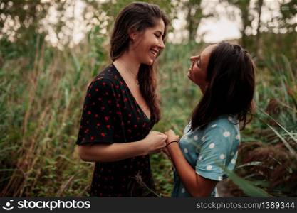 Two young lesbians look at each other an smiling in the field wearing dresses