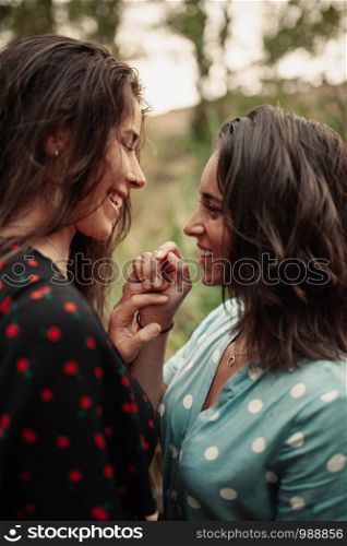 Two young lesbians look at each other holding their hands in the field wearing dresses