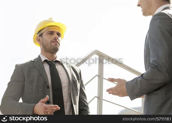Two young male engineers discussing on stairway against clear sky