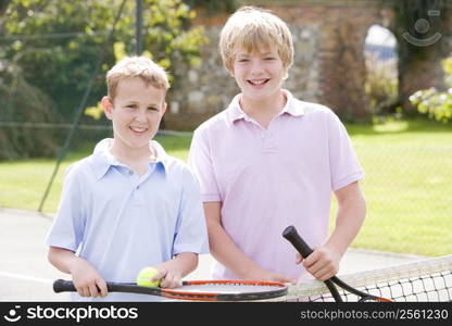 Two young male friends with rackets on tennis court smiling