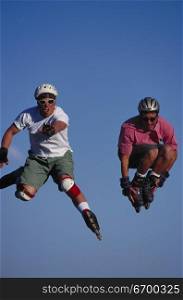 Two young male roller bladders jumping in the air