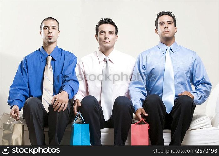 Two young men and a mid adult man sitting on a couch holding shopping bags