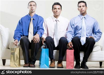 Two young men and a mid adult man sitting on a couch holding shopping bags