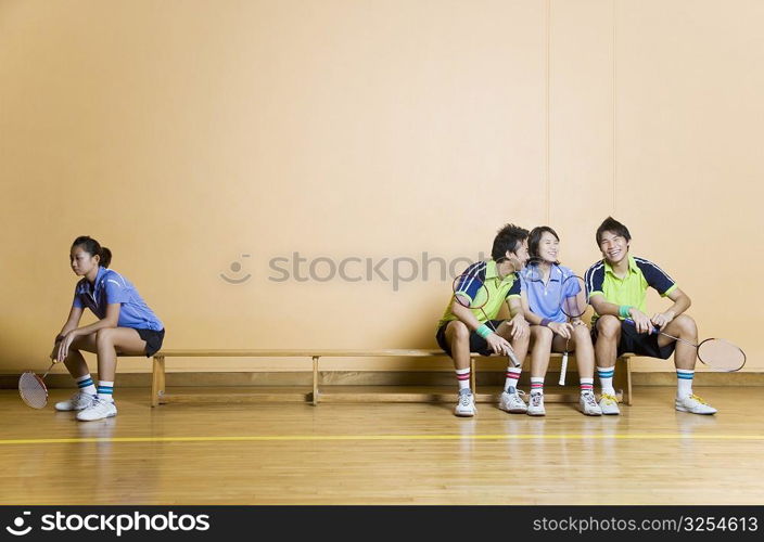 Two young men and a young woman sitting side by side on a bench with another young woman sitting at other corner