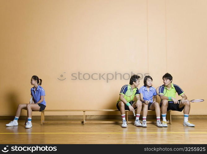 Two young men and a young woman sitting side by side on a bench with another young woman sitting at other corner