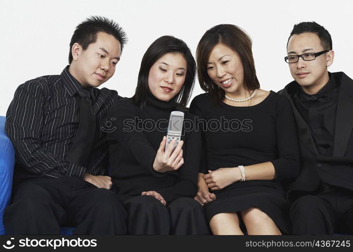 Two young men and two young women sitting on a couch looking at a mobile phone