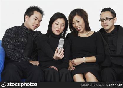 Two young men and two young women sitting on a couch looking at a mobile phone