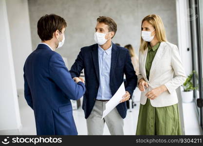 Two young men and woman discussing with paper in hands indoors in the office with young people works behind them