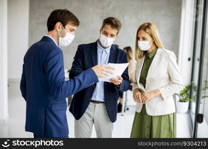 Two young men and woman discussing with paper in hands indoors in the office with young people works behind them