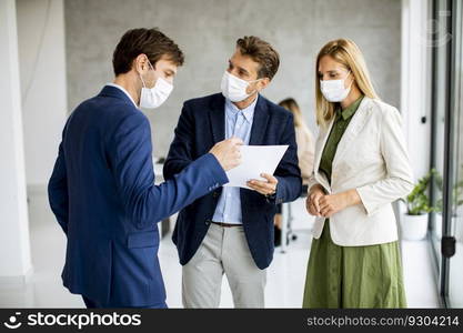 Two young men and woman discussing with paper in hands indoors in the office with young people works behind them