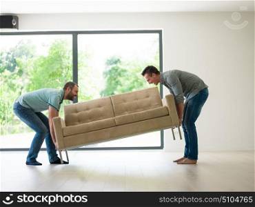 two young men carry the sofa in front of window