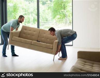two young men carry the sofa in front of window