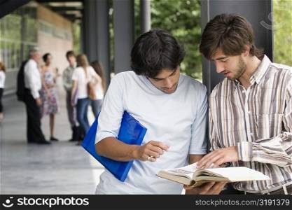Two young men looking at a book in a corridor