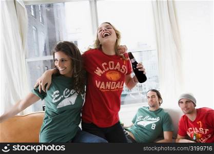 Two young men lying on a couch with two young women drinking beer and dancing