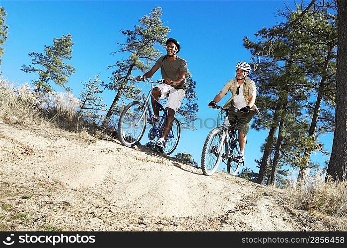 Two Young Men mountain biking on track through field low angle view.