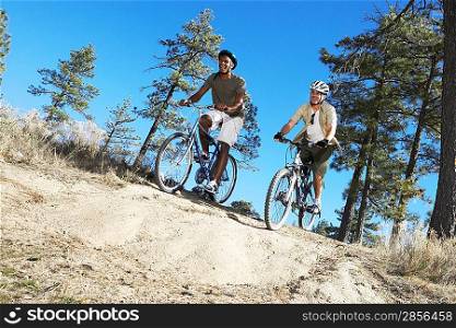 Two Young Men mountain biking on track through field low angle view.