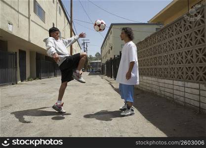 Two young men playing with a soccer ball on the street