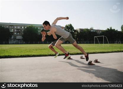 Two young men running on race track. Male professional athletes running on athletics race track.. Low section shot of male athletes starting a race in stadium with sunflare.