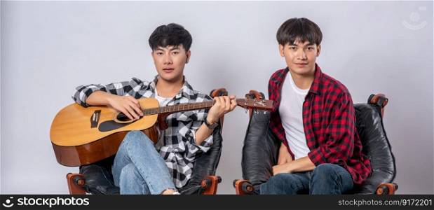 Two young men sat on a chair and played guitar.