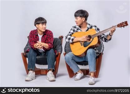 Two young men sat on a chair and played guitar.
