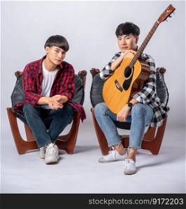 Two young men sitting in a chair holding a guitar.