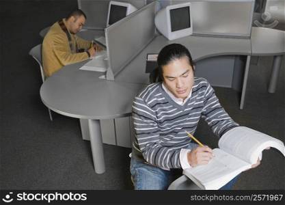 Two young men sitting in a computer lab and writing