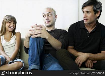 Two young men sitting on a couch and looking at a girl laughing