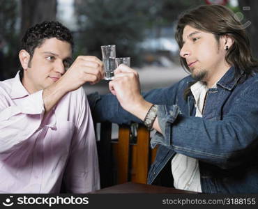 Two young men toasting with shot glasses of tequila