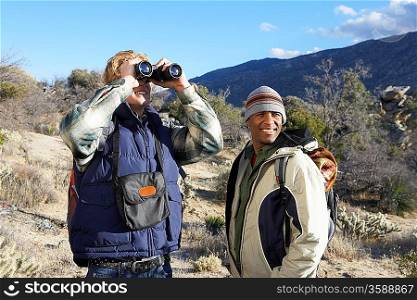 Two Young Men Using Binoculars While Hiking in Hills