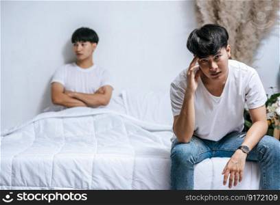 Two young men were angry on the bed and the other sat at the edge of the bed and was stressed.