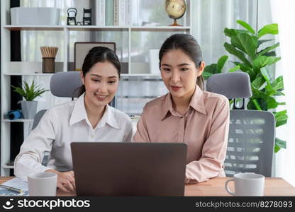 Two young office lady colleagues collaborating in modern office workspace, engaging in discussion and working together on laptop, showcasing their professionalism as modern office worker. Enthusiastic. Two young businesswoman work together in office workspace. Enthusiastic