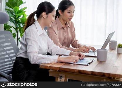 Two young office lady colleagues collaborating in modern office workspace, engaging in discussion and working together on laptop, showcasing their professionalism as modern office worker. Enthusiastic. Two young businesswoman work together in office workspace. Enthusiastic