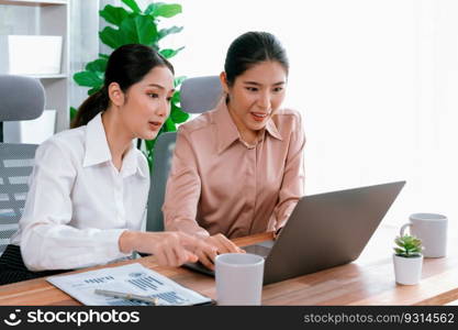 Two young office lady colleagues collaborating in modern office workspace, engaging in discussion and working together on laptop, showcasing their professionalism as modern office worker. Enthusiastic. Two young businesswoman work together in office workspace. Enthusiastic